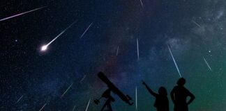 Silhouetted people stargazing with telescope under meteor shower.