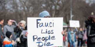 Person holding sign that reads Fauci Lies People Die