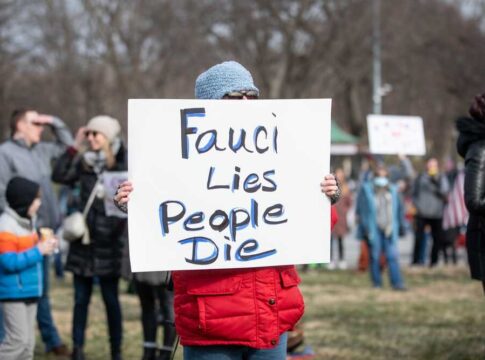 Person holding sign that reads Fauci Lies People Die