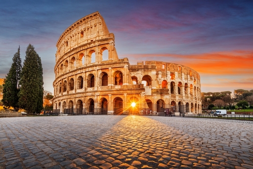 The Colosseum in Rome at sunset with a glowing sun in the background