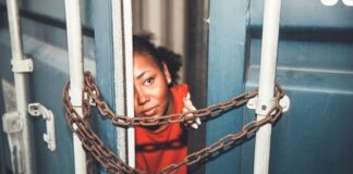 Person peeking through chained gap of a shipping container.