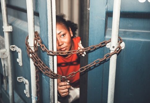 Person peeking through chained gap of a shipping container.