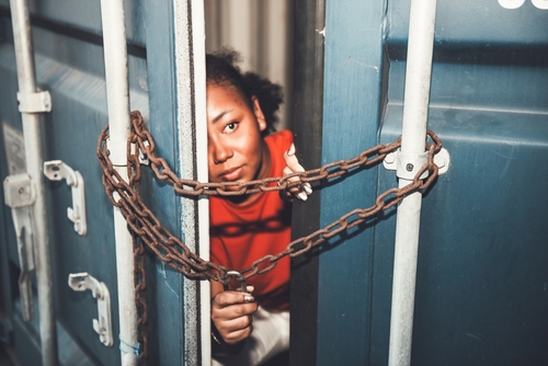 Person peeking through chained gap of a shipping container.