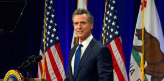 Governor Gavin Newsom speaks at podium with flags behind.