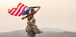 Child on soldiers shoulders holding American flag.