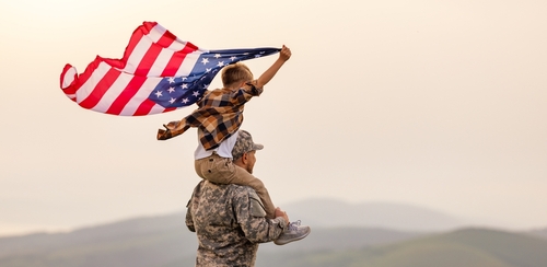 shutterstock_2168238715.jpg featured image Child on soldiers shoulders holding American flag.