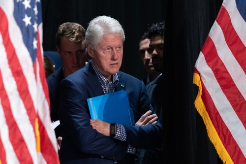 shutterstock_2222838159 (2).jpg featured image Bill Clinton standing between American flags with a folder.