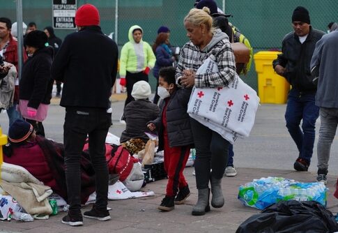 People at an outdoor relief station with Red Cross supplies.