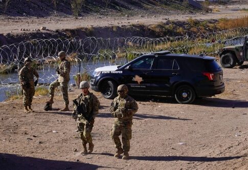 Military personnel and law enforcement officers near a border area with vehicles and barbed wire