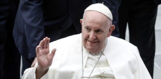 A man in white clerical robe smiling and waving.
