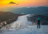 Person pointing at UFOs in snowy mountain landscape.