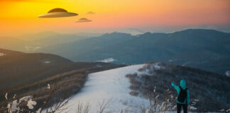 Person pointing at UFOs in snowy mountain landscape.