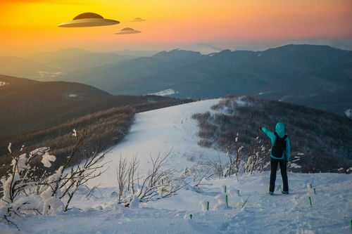 shutterstock_2261586029.jpg Person pointing at UFOs in snowy mountain landscape.