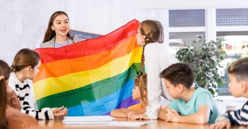 Teacher showing rainbow flag to children in classroom.