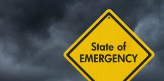 Yellow "State of Emergency" sign, dark stormy sky.