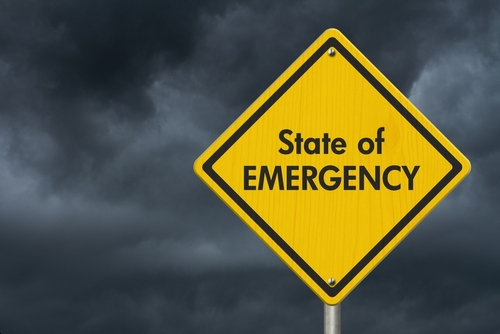 shutterstock_2264564769.jpg featured image Yellow "State of Emergency" sign, dark stormy sky.
