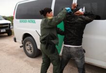 Border Patrol agent detains a man against a vehicle.