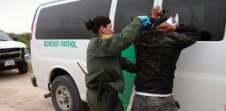 Border Patrol agent detains a man against a vehicle.