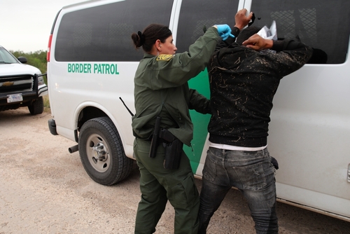 shutterstock_2265137295.jpg featured image Border Patrol agent detains a man against a vehicle.