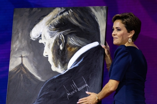 shutterstock_2270823761 (1).jpg featured image A woman holding a painting of Donald Trump.
