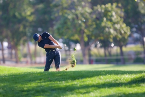 A person golfing on a green course, mid-swing.