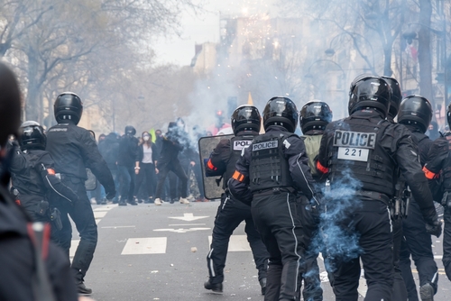 Police officers in riot gear confronting protesters with tear gas.