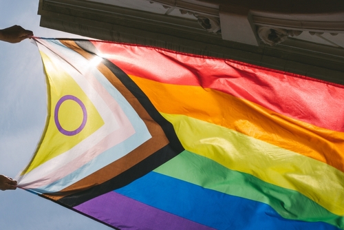 Progress Pride flag held up against the sky.
