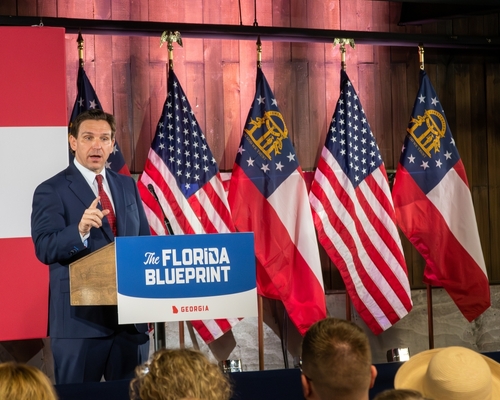 shutterstock_2297083921.jpg featured image Man speaking at Florida Blueprint event with American flags.