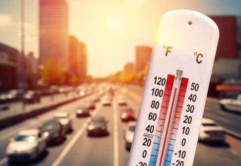 Thermometer showing high temperature in busy city traffic.