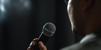 Person holding a microphone, speaking or singing.