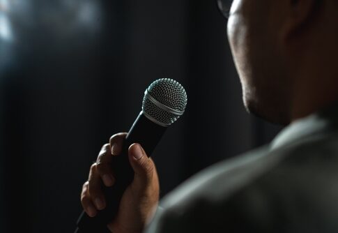 Person holding a microphone, speaking or singing.