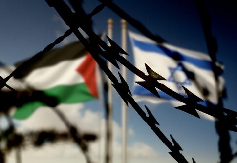 Barbed wire with Palestinian and Israeli flags blurred in background.