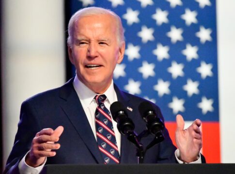 Man speaking at podium in front of flag