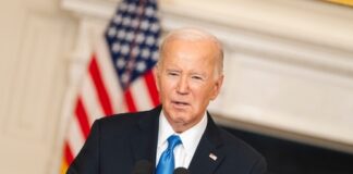 Man speaking at podium with American flag in background.