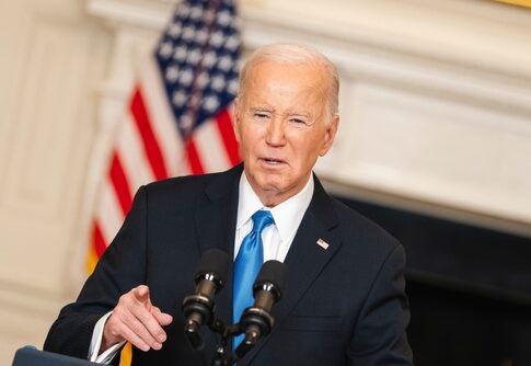 Man speaking at podium with American flag in background.