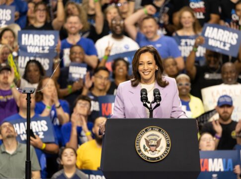 Woman speaking at podium with cheering crowd behind