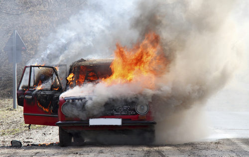 A car engulfed in flames with smoke billowing out