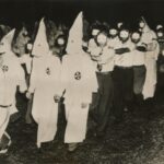 Ku Klux Klan members marching in white robes and hoods.