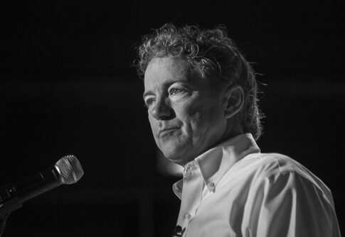 A man with curly hair speaking into a microphone in black and white