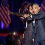 Two people onstage, smiling and pointing at something.