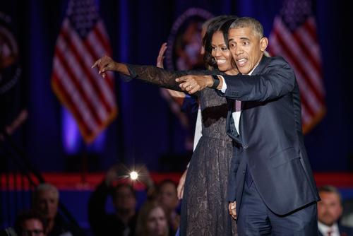 Two people onstage, smiling and pointing at something.
