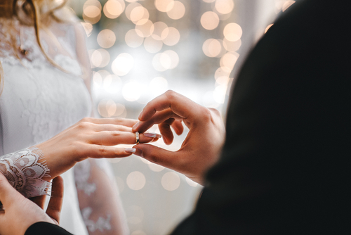 shutterstock_589431530.jpg featured image Groom placing ring on bride's finger at wedding.
