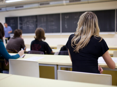 Students seated in a classroom listening to a teacher at the chalkboard