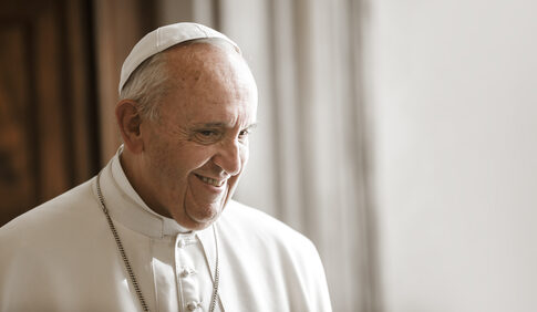 A smiling Pope Francis in white papal attire.