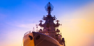 Battleship and submarine in a harbor at sunset.