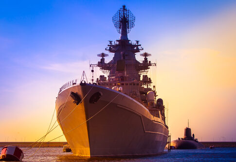 Battleship and submarine in a harbor at sunset.