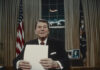 A man in a suit holding a blank sheet of paper in a presidential office