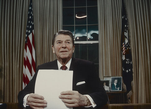 A man in a suit holding a blank sheet of paper in a presidential office