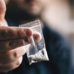 Person holding a small bag of white powder.