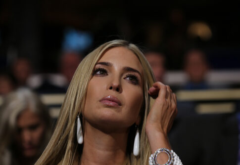 A woman with long blonde hair and earrings looking thoughtfully during an event